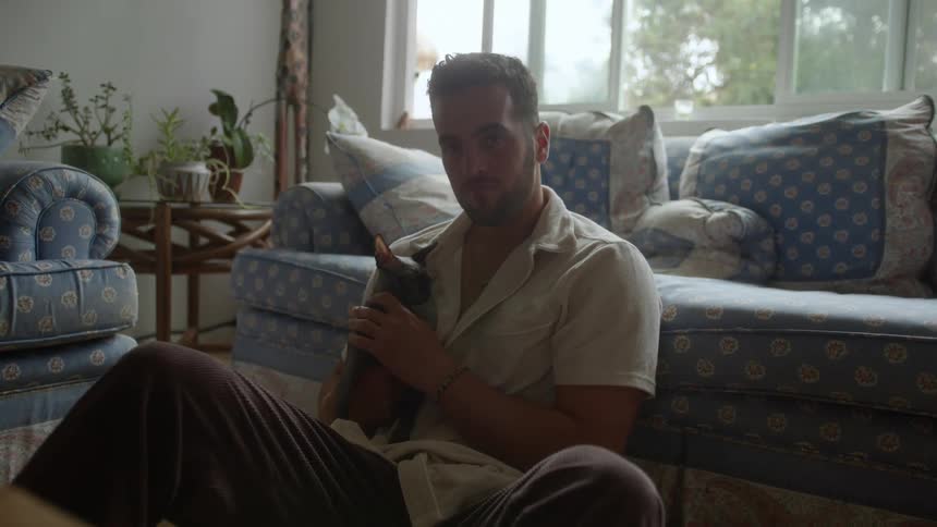 Bearded man sitting on living room floor and holding a cat