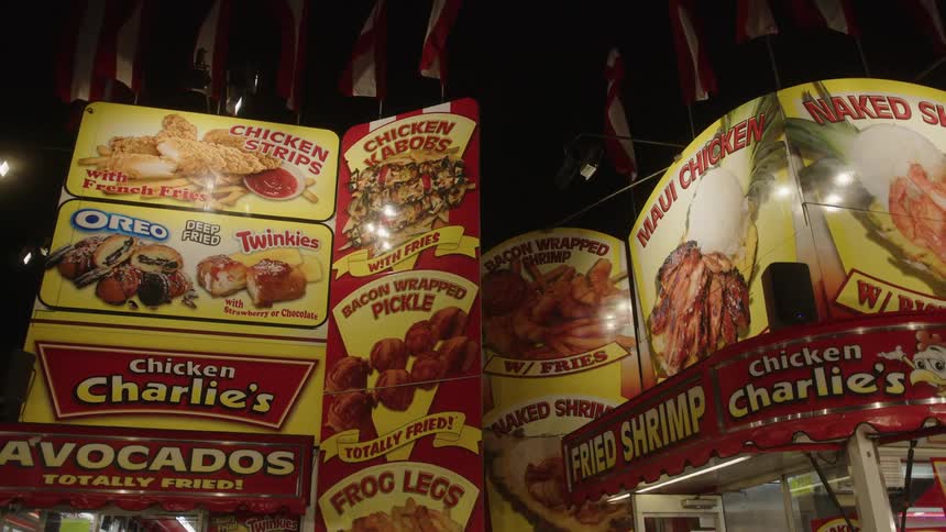 Illuminated facade of a trade show booth with vibrant eyecatching signs promoting a variety of fried and exotic foods