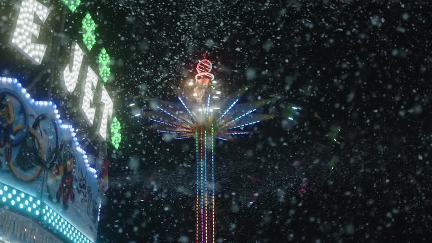Amusement park ride in operation with people suspended in the air at night on a snowy day