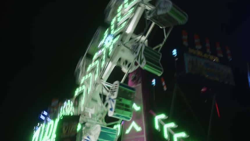 An amusement park ride spins around and flashes its lights as its chairs spin