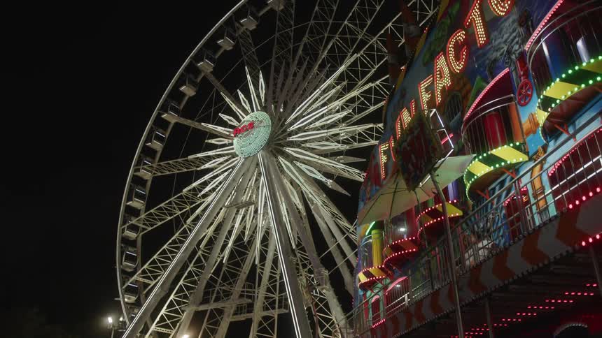 A brightly lit ferris wheel and a colorful amusement ride at night