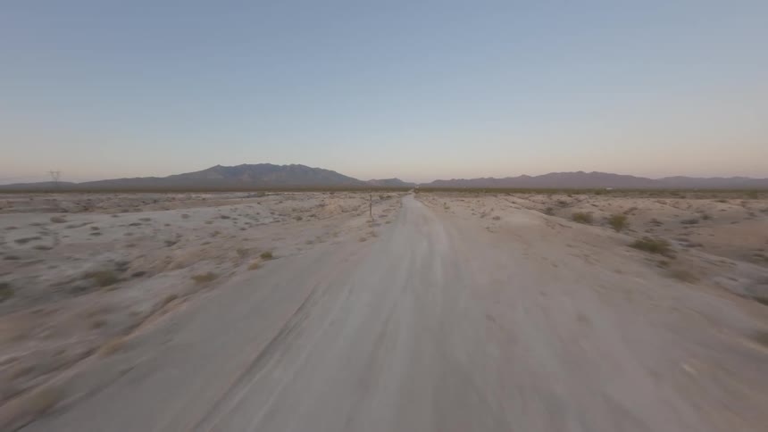 Aerial view of a dirt road in a desert environment with sparse vegetation and mountains on the horizon