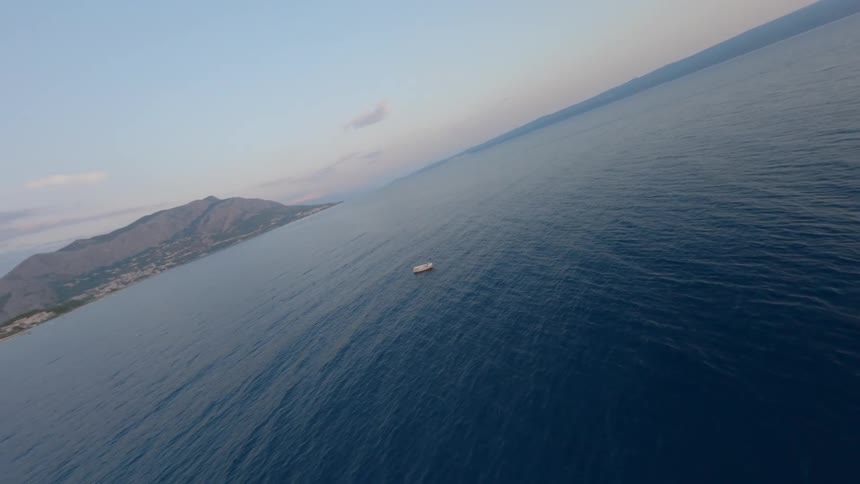 A small boat drifts peacefully on the calm blue water with a mountainous coastline in the distance