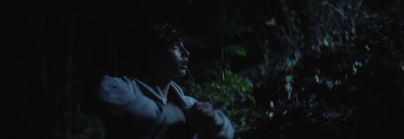 Boy outdoors in a forest at night putting on a jacket