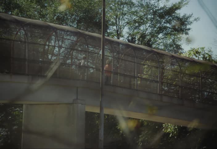 Two teenagers riding a skateboard over an overpass