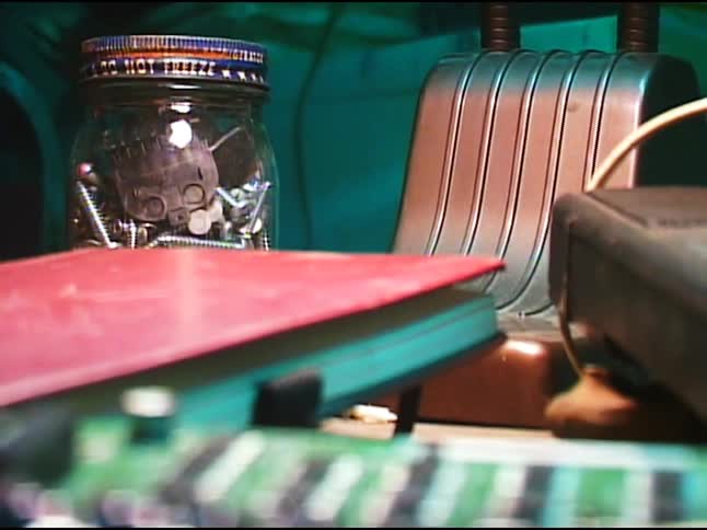 The image shows a cluttered desk with a jar of screws a red notebook an old radio and various electronic components scattered across its surface