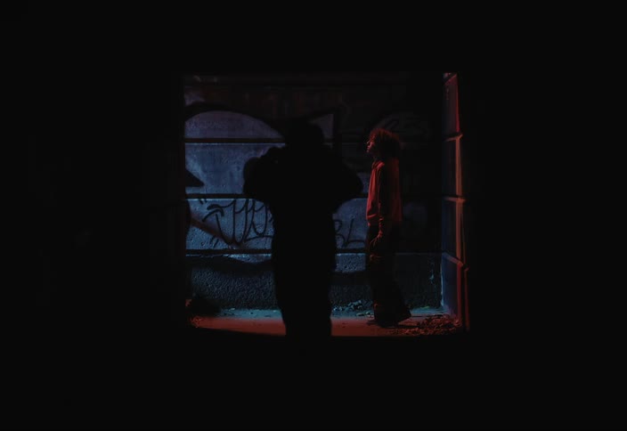Two people in a dark hallway with graffiti talking