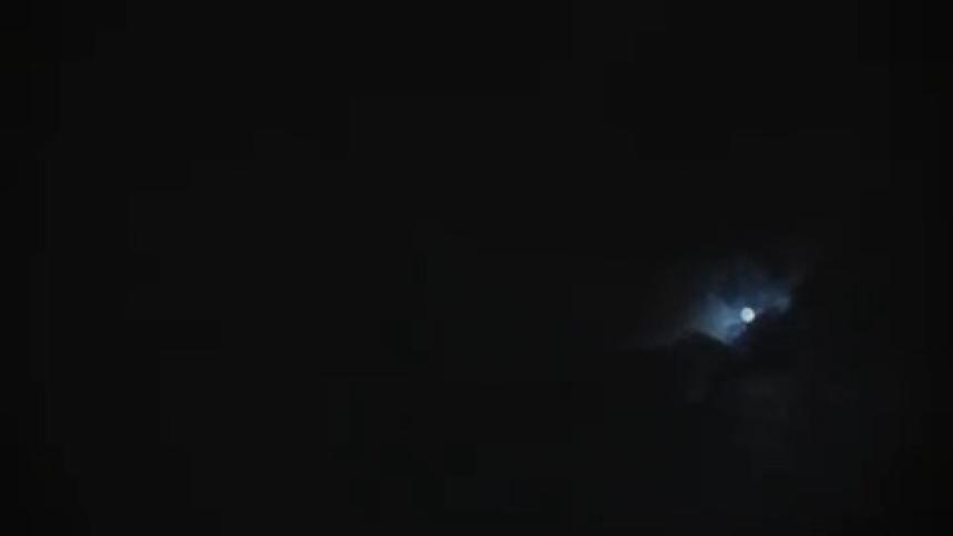 A lowlight shot captures the moon partially obscured by dark clouds that are moving swiftly across the night sky