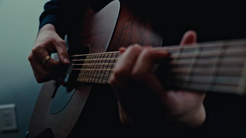 A man wearing a black sweater strums the acoustic guitar