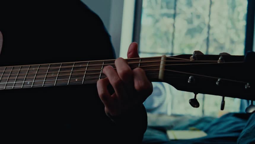 A close up shot shows a persons hands strumming an acoustic guitar transitioning between different angles showcasing the instrument and the players technique