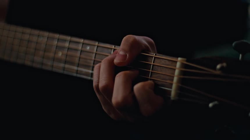 Man wearing a sweater strums the acoustic guitar