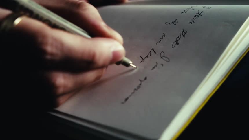 A mans hand adorned with a ring carefully writes down notes in a notebook