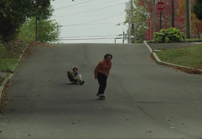 Boy going down a street doing skateboard tricks and another boy going down a skateboard also with a camera