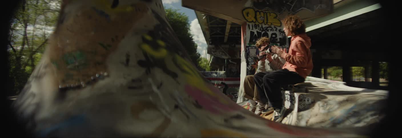 Boy sitting on a skate park being filmed by another boy with a professional camera