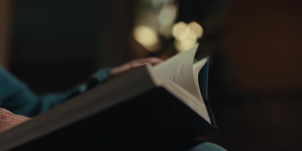 Elderly person sits at home and pages through a hardback book