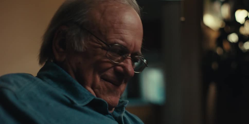 Elderly man smiles while sitting at home and reading a book