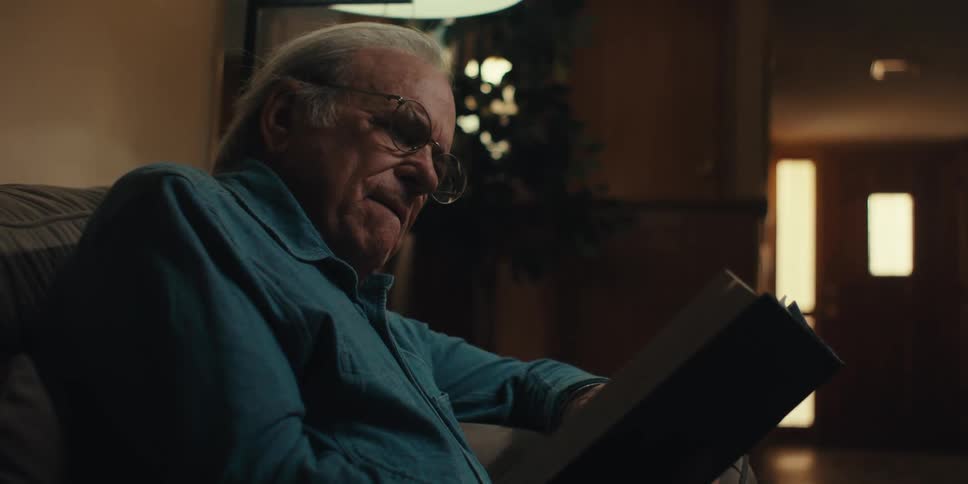 Elderly man sits in the living room at home while reading a hardback book