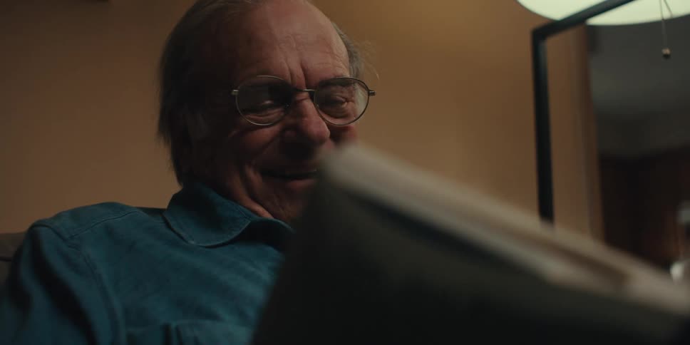Close up of an elderly man sitting at home laughing while reading a book