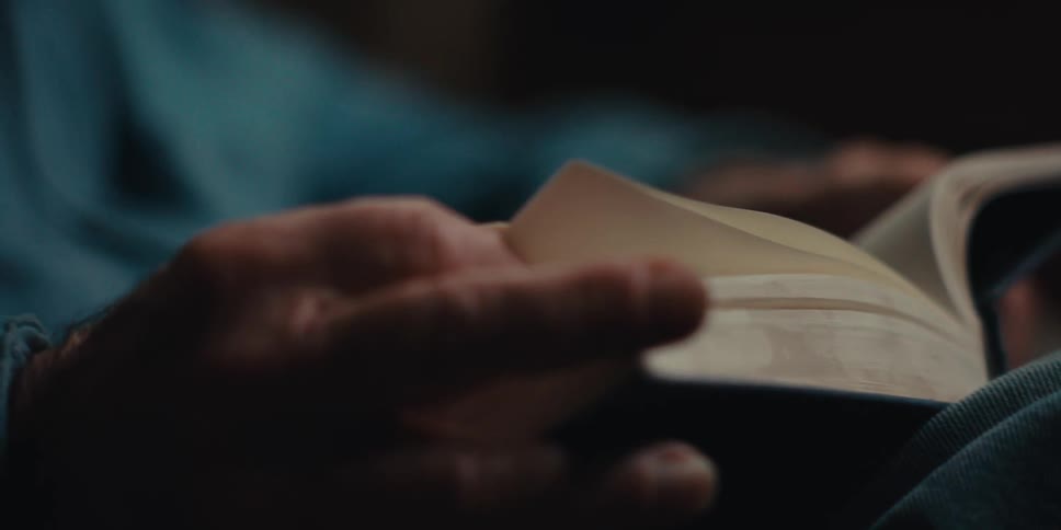 Elderly man sits at home concentrating on the book he is reading