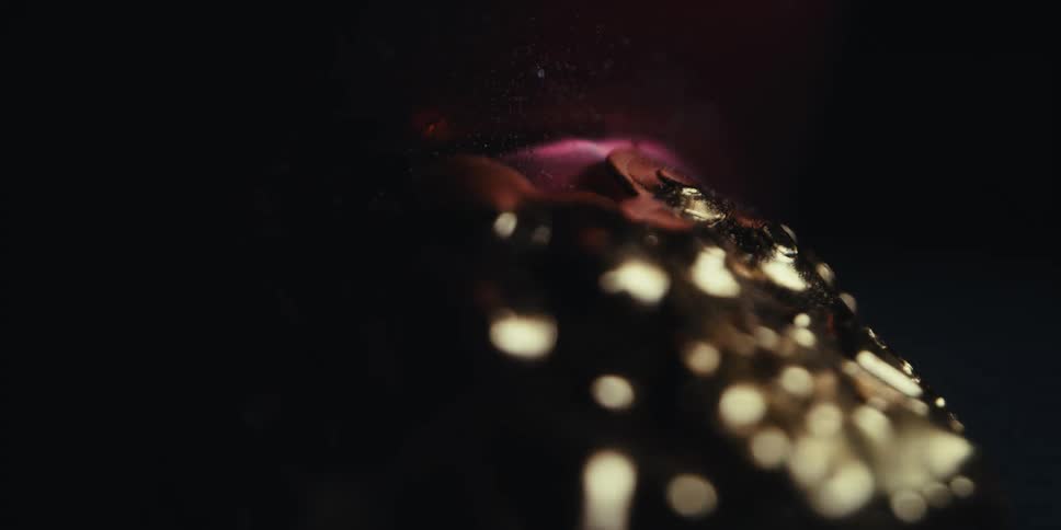Light shines briefly on a gold metal object then fades to black