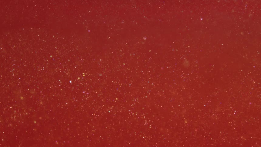 Small shiny balls moving in a dense reddish liquid