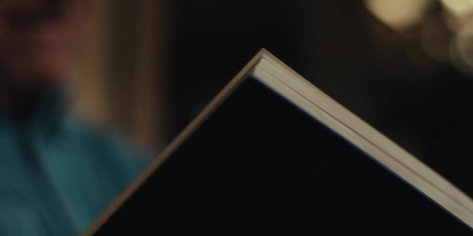 An elderly man wearing glasses and a blue shirt reads a book while sitting on the couch in the living room