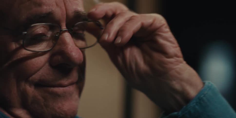 Elderly man in a blue shirt wears glasses and reads a book
