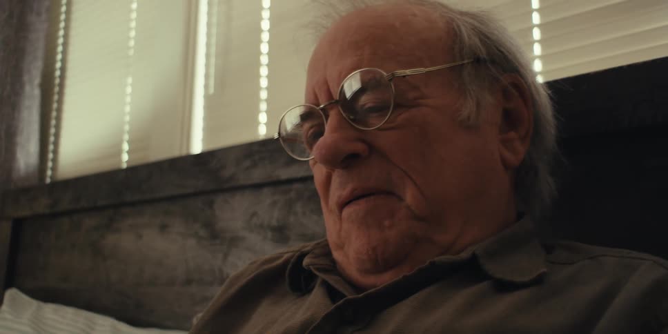 Closeup of an elderly man wearing glasses reading a book on a couch at home