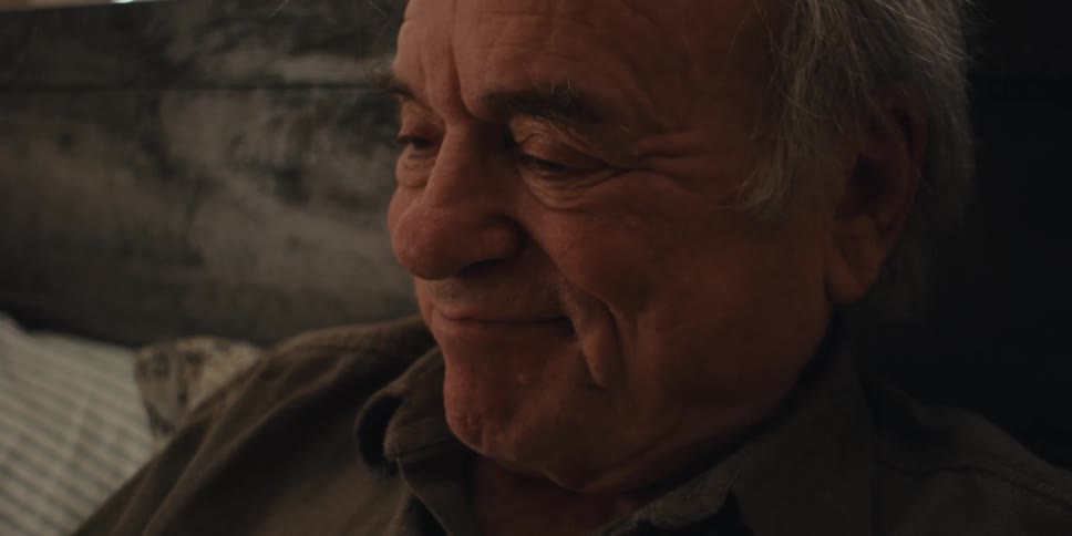 Elderly man sitting on bed and putting on glasses