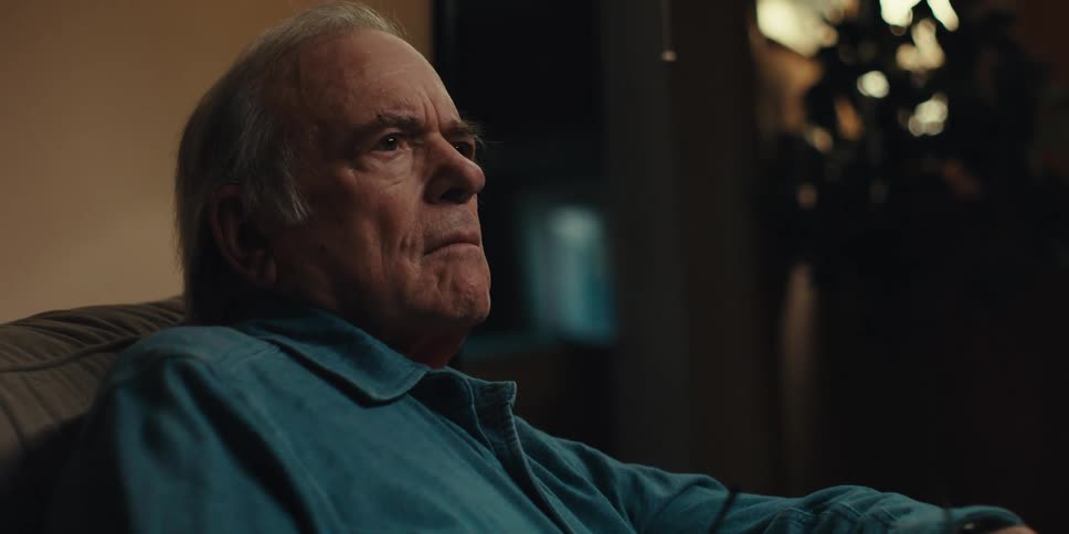 An elderly man in a blue shirt reading a book takes off his glasses thoughtfully