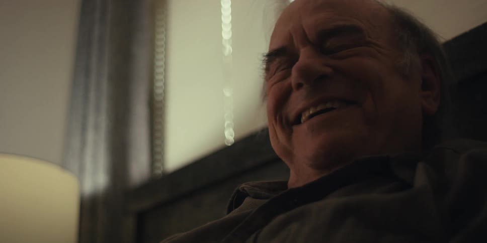 Elderly man lying in bed with happy facial expression and taking off his glasses