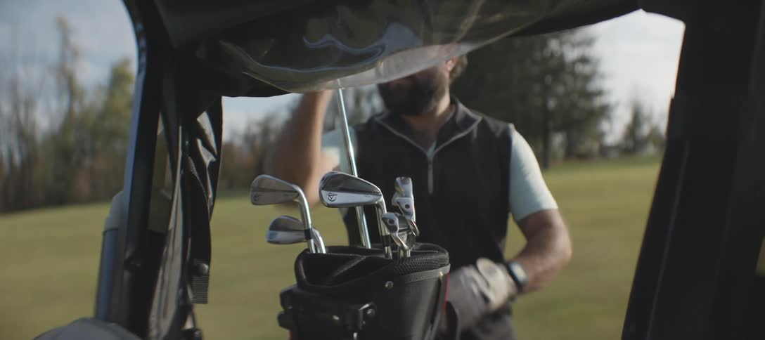 Man in cap on a field picking up a golf club