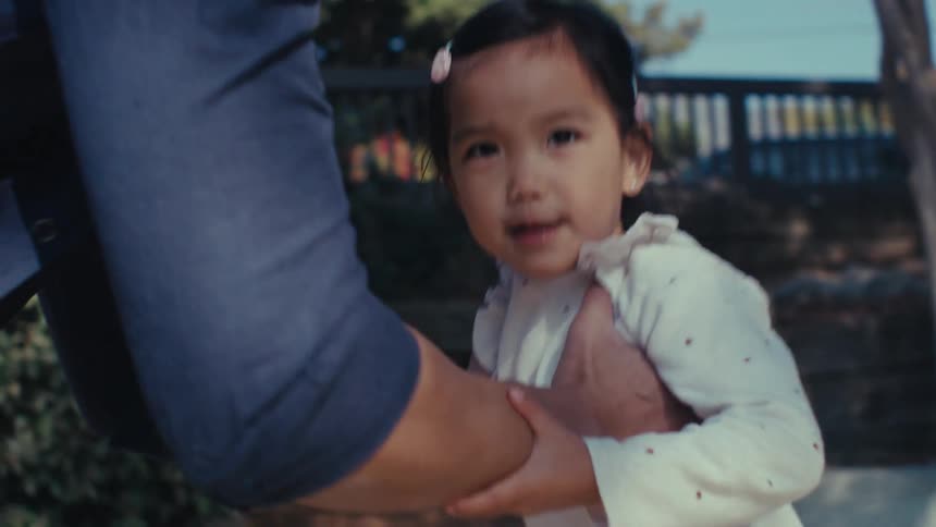 Little girl running into her fathers lap who picks her up and gives her a kiss and a hug