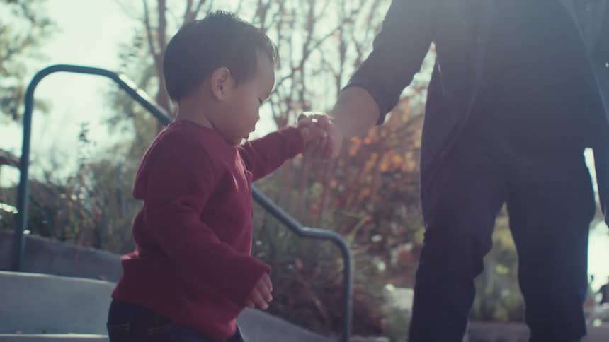 Father helps his son down outdoor stairs then the boy approaches playground equipment on an autumn day