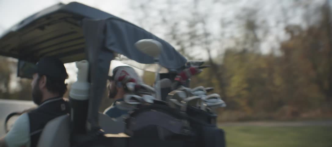 Two golfers taking off on a golf cart on a golf course