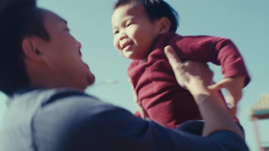 Father picking up his son as he goes down a slide and they both clap their hands