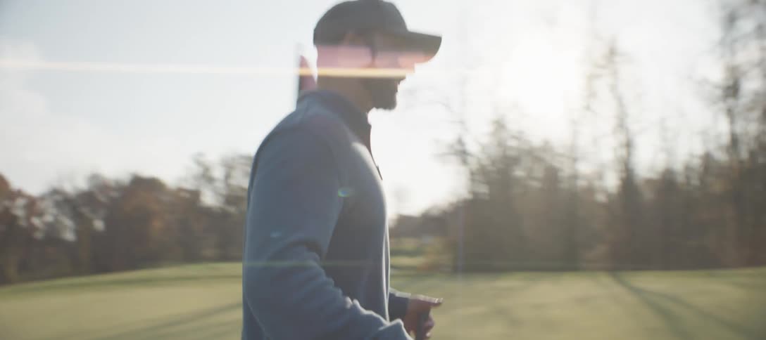 A golfer walks across a golf course on a sunny autumn day