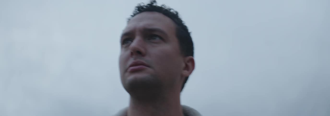 Close up of the face of a man standing under a cloudy sky
