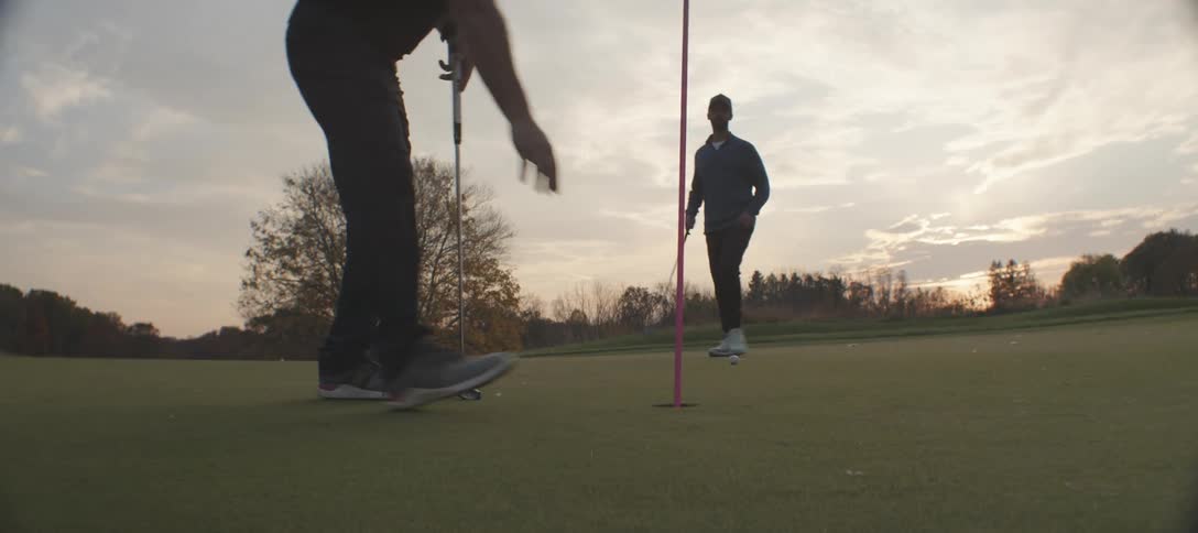 Two men playing golf on a course in the late afternoon