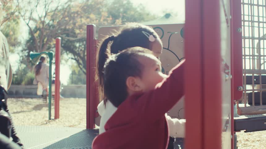 Mother outdoors with her two little children playing on a playground