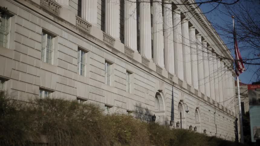 A large building with several pillars has an american flag on a poll next to it