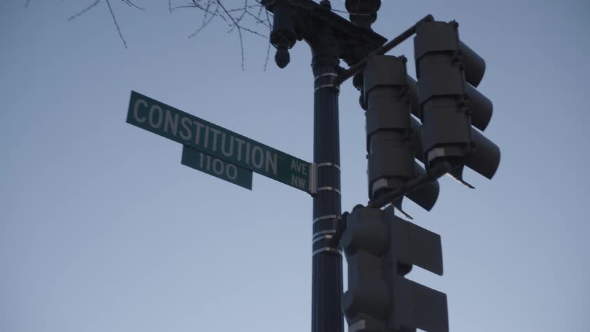 Traffic light in a city with a lamppost and a nameplate against a blue sky