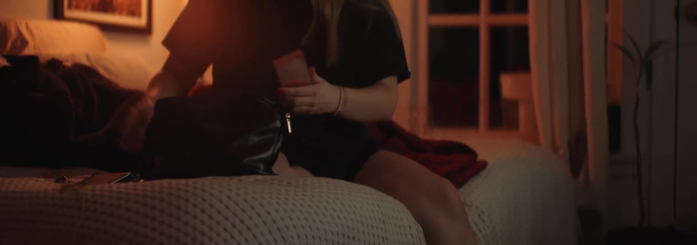 A woman wearing black shorts and a shirt searches through her bag for makeup in her room at night