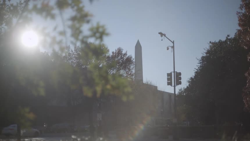 Street of a metropolis with a public bus passing by and a historic pillar in the background
