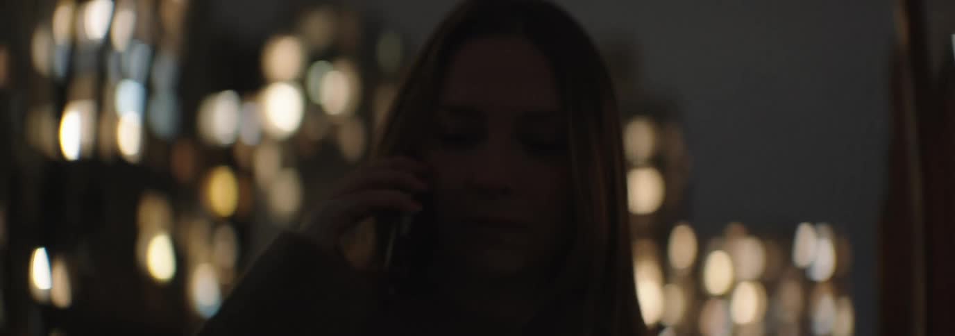 Woman talking on the phone is silhouetted against the illuminated tall buildings at night