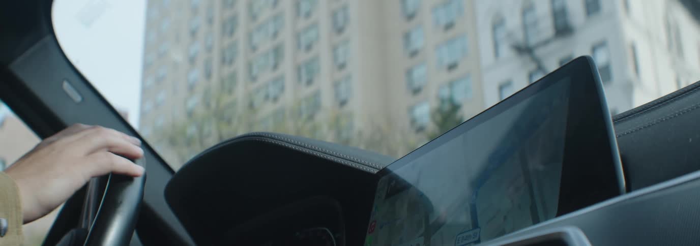 A person driving a car with a large folded down dashboard screen displaying a city map