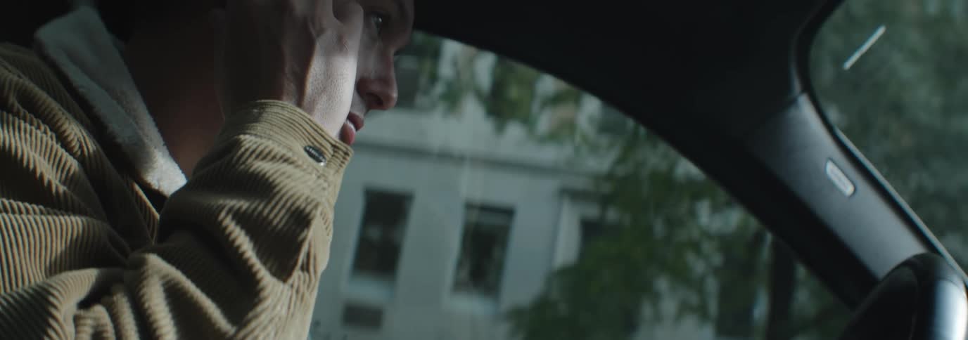 A man wearing a brown corduroy jacket drives a car in the city street