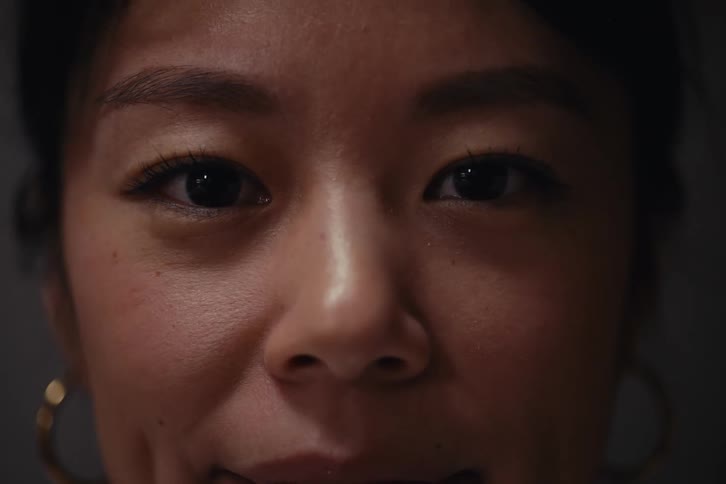 A womans face focusing on her eyes and upper face with soft lighting that highlights her natural skin texture and subtle makeup complemented by gold hoop earrings