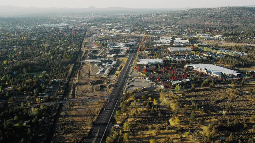 Aerial panorama of a long highway with a factory in the background in an urban area surrounded by greenery and mountains on the horizon