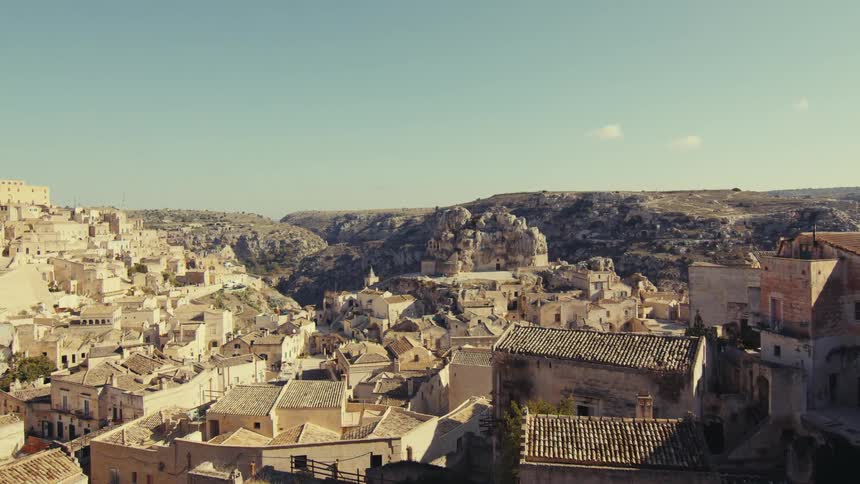 A scenic view of a historic town built on rugged terrain with stone buildings and tiled rooftops cascading down the hillside set against a backdrop of cliffs and a clear blue sky